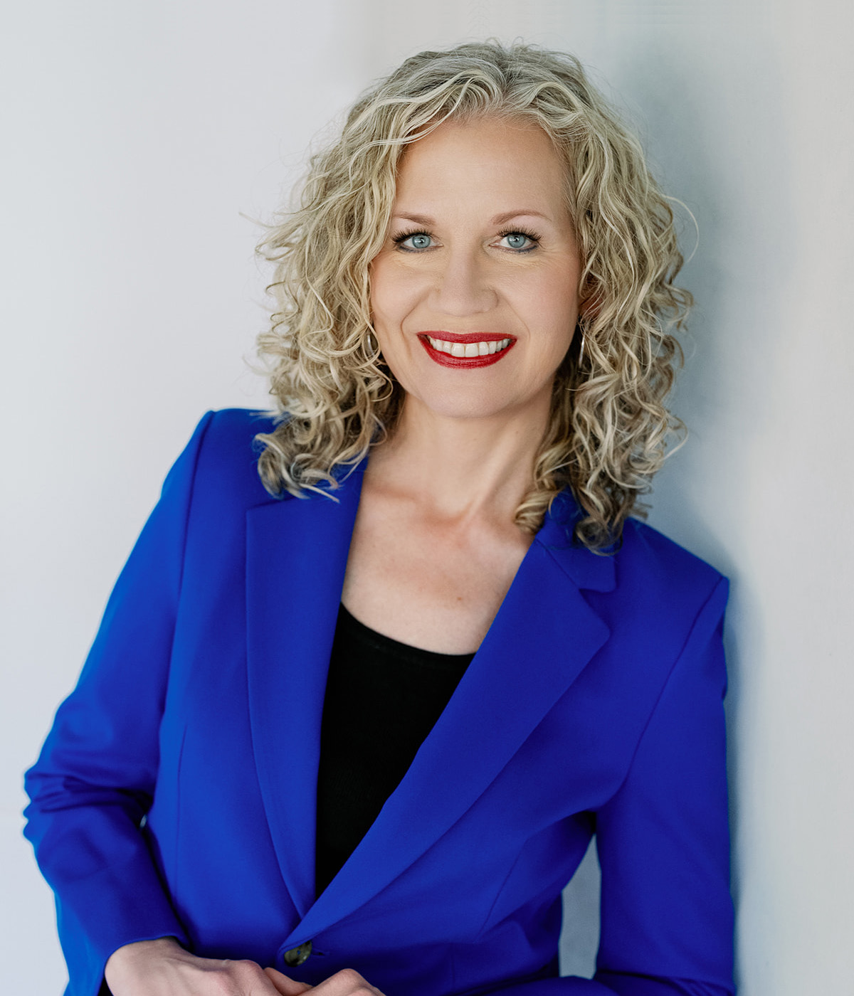Woman with curly blonde hair in a blue blazer smiling confidently.
