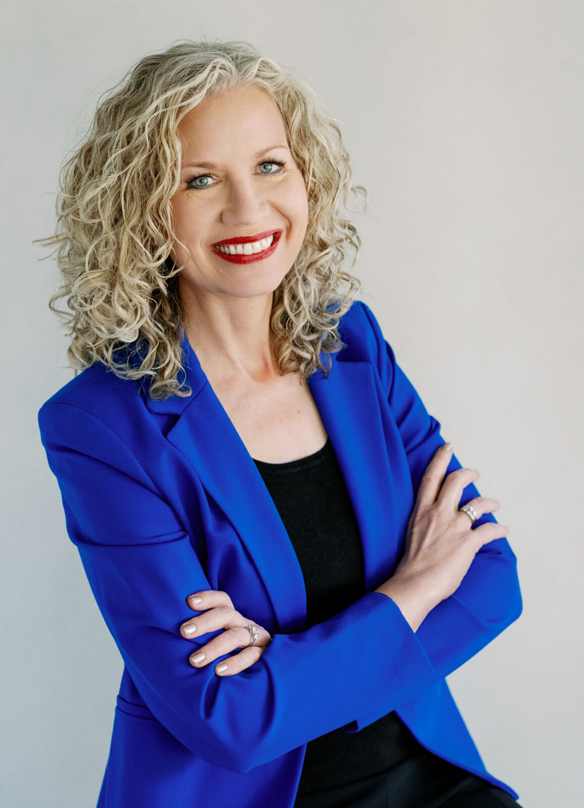 Confident woman with curly blonde hair in a blue blazer smiling.